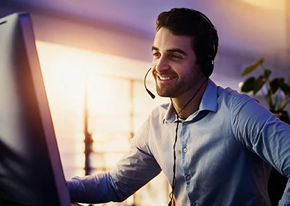 Profesional de atención al cliente sonriendo con auriculares frente al ordenador