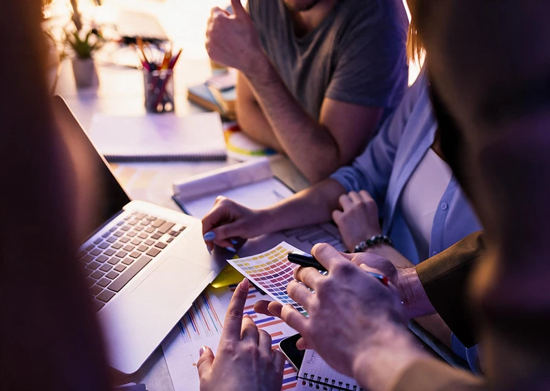 Equipo revisando una gu&iacute;a de colores y bocetos junto a un port&aacute;til en una reuni&oacute;n de dise&ntilde;o web