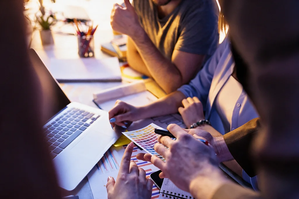 Equipo revisando una guía de colores y bocetos junto a un portátil en una reunión de diseño web